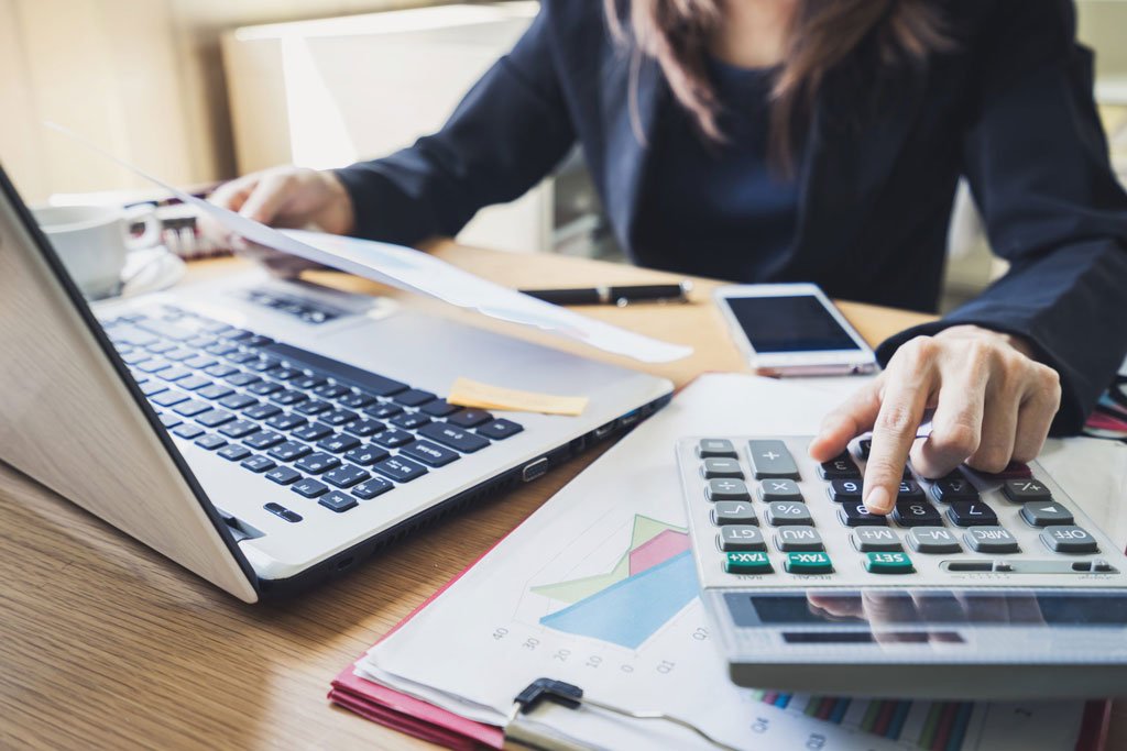 Person using a calculator and laptop to process invoices.